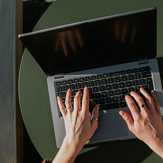 Zu sehen ist ein Laptop und tippende Hände.
