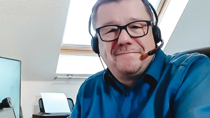 Ein Trainer während einer Online-Weiterbildung mit Headset schaut in de Kamera.