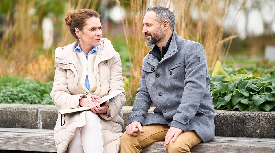Zu sehen ist eine Coachin und ein Coachee, sie sitzen draußen und führen ein Gespräch